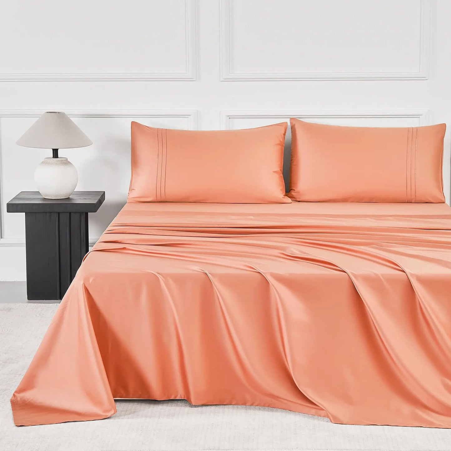 JELLYMONI Soft Cool Cotton Sateen Sheets in vibrant coral, creating a warm and inviting bed atmosphere with coordinating pillows and a lamp.